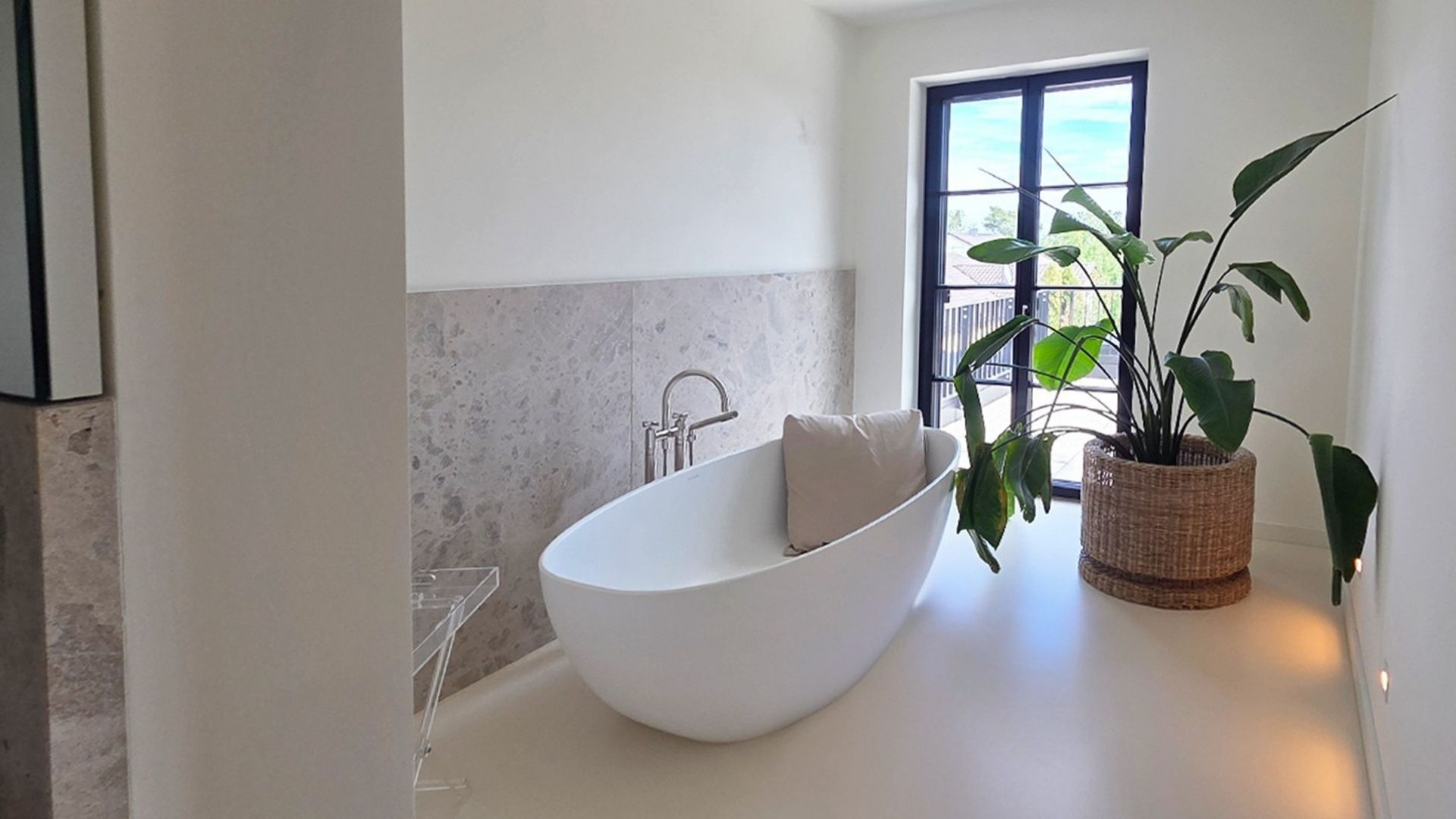 Elternbad mit freistehender Wanne vor Natursteinwand und Fenstertür zur Dachterrasse