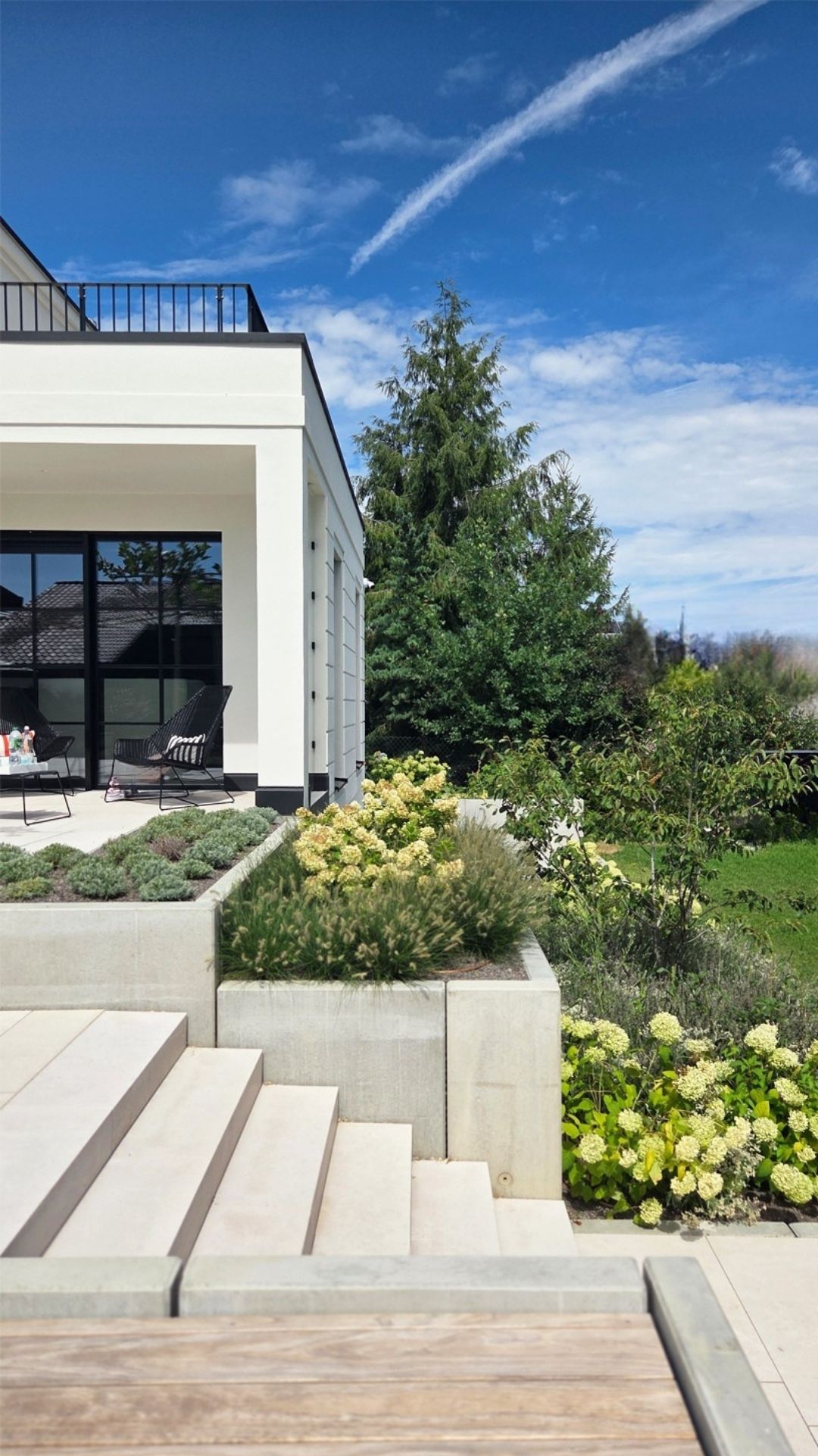 Gartenseite mit Natursteintreppe, Pflanzinseln und überdachter Terrasse